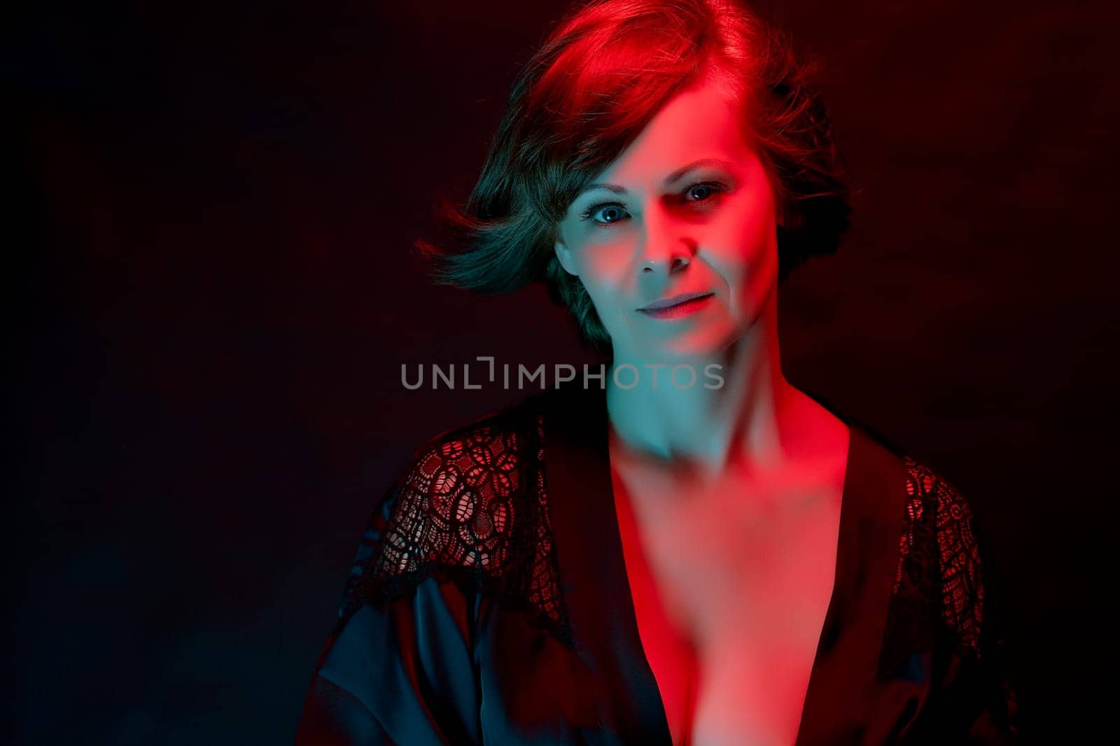 Beautiful attractive young woman posing in satin bathrobe in neon light in the studio.