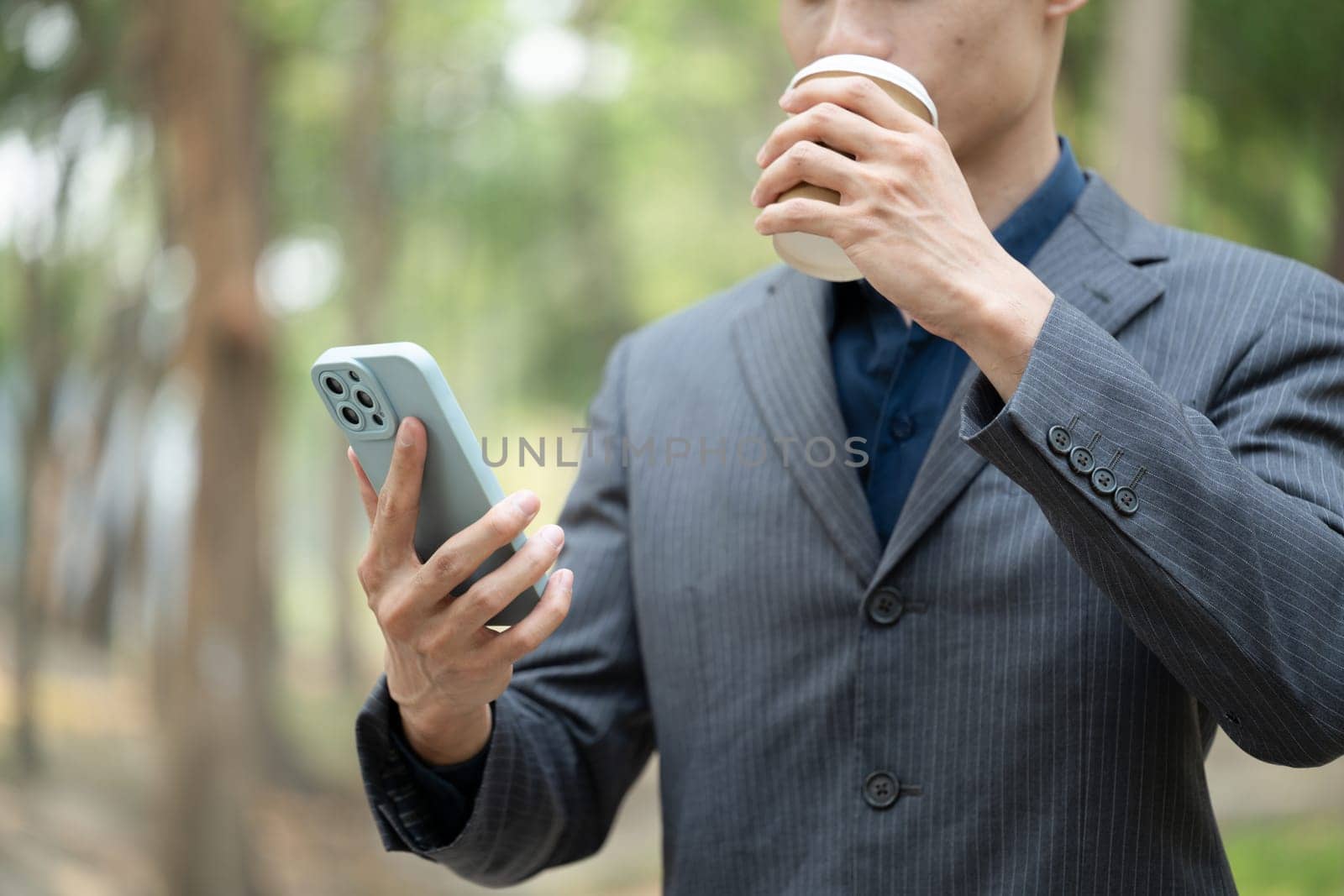 Cropped shot of businessman in formal suit drinking coffee and using mobile phone outdoor.