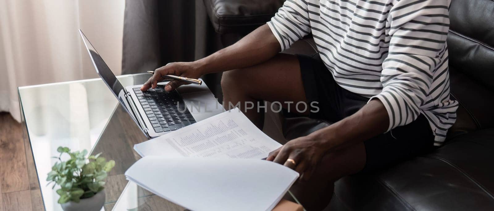 African American man working with laptop computer remote while sitting at sofa in living room. Black guy do freelance work at home office.