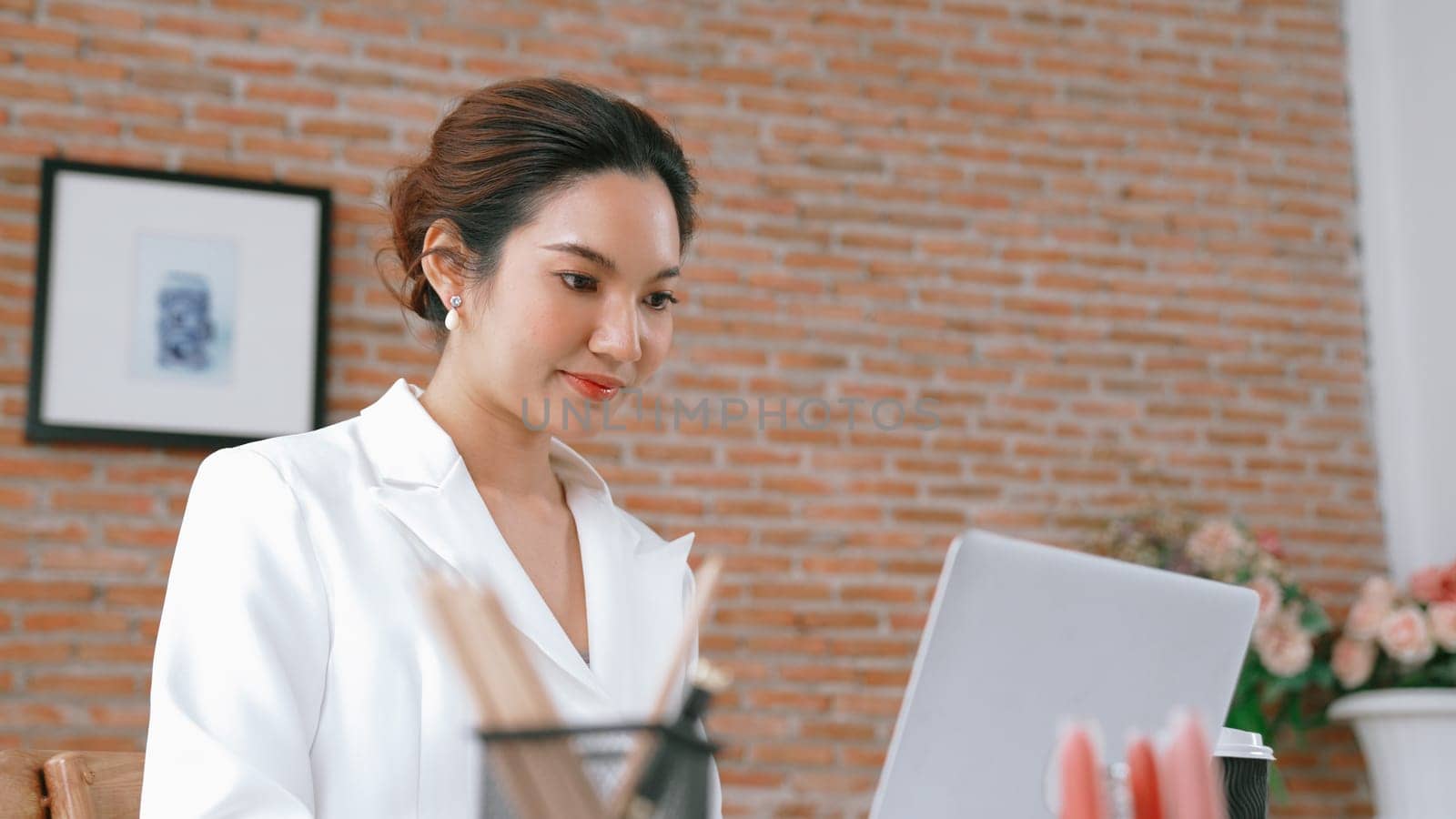 Young businesswoman sitting on the workspace desk using laptop computer for internet online content writing or secretary remote working from home. Vivancy