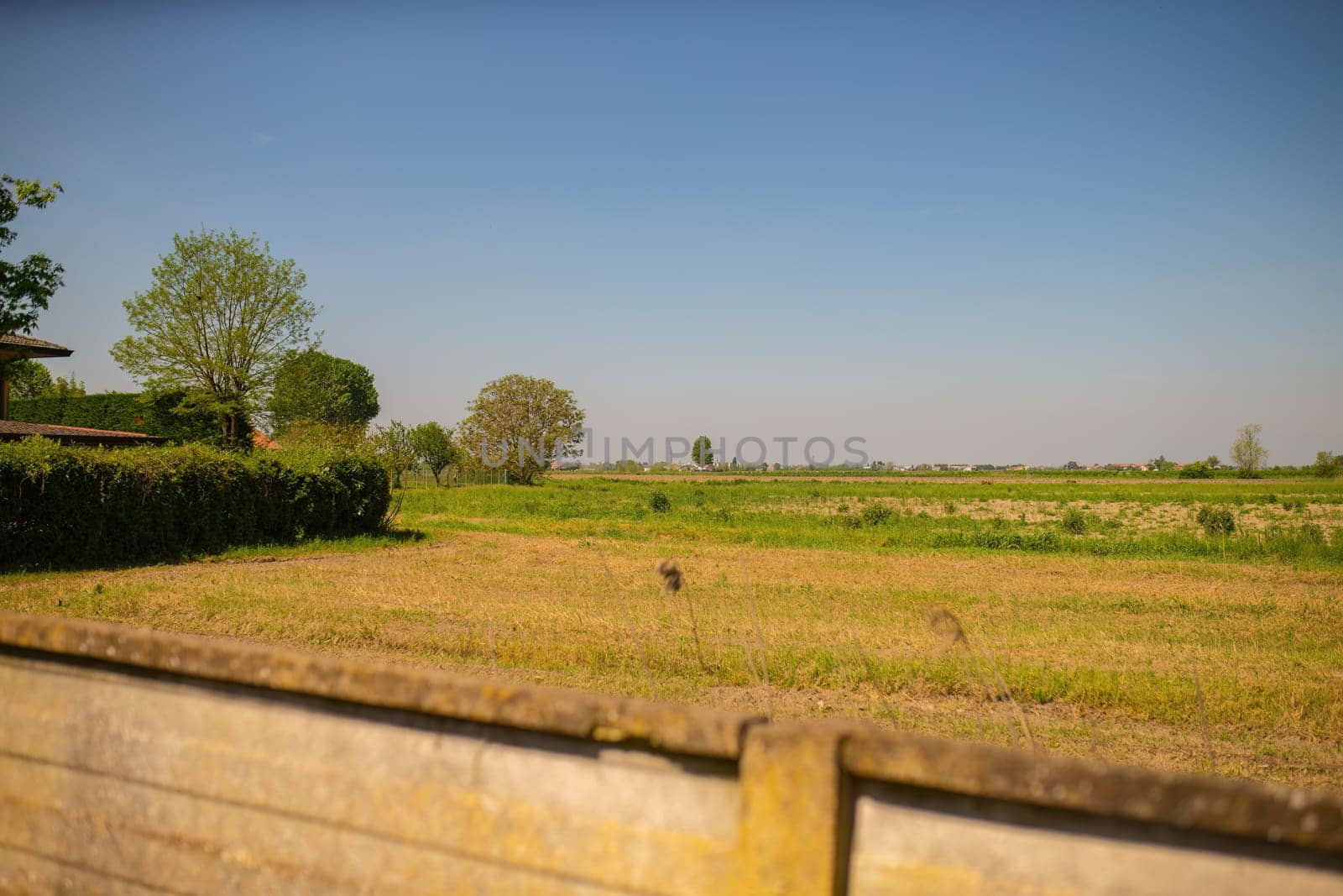 A wooden fence stands in the foreground of a lush grassy field under a clear sky.