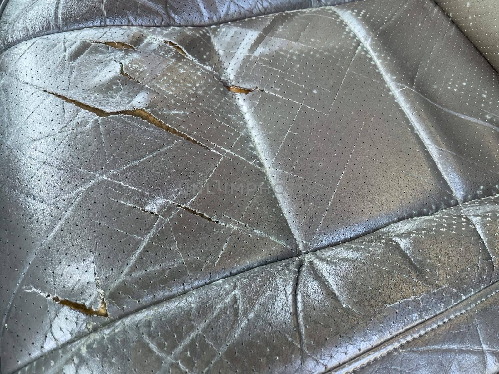 Close-up of a distressed and torn leather seat inside a car.