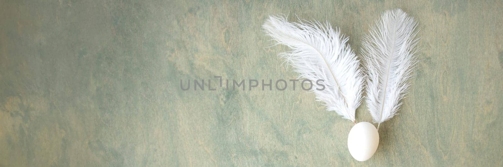 banner of Easter background, egg and white feathers in the form of a hare on a green wooden background
