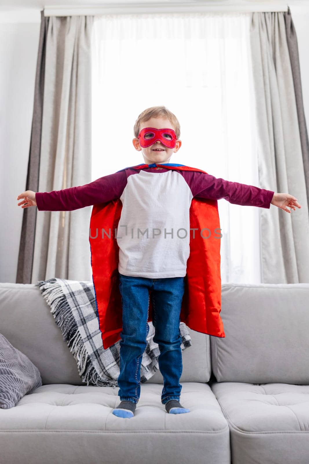 Child in superhero outfit with cape and mask, home interior. Candid lifestyle photography for poster and banner.