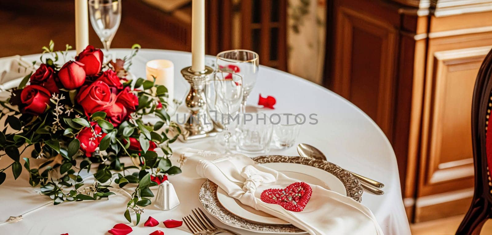 Festive table setting with cutlery, candles and beautiful red flowers in a vase.