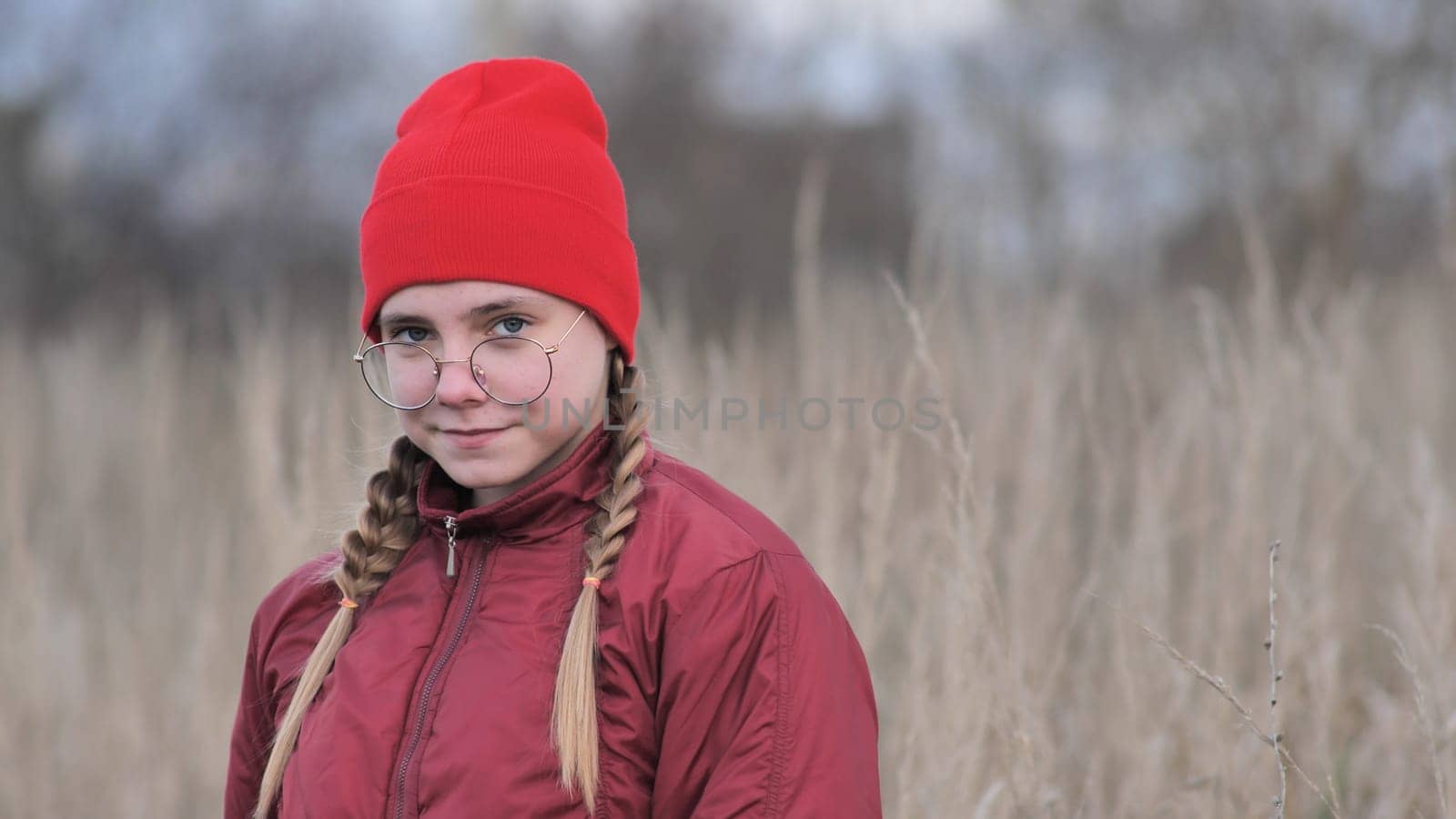 A teenage girl in red clothes touching dry grass in late fall