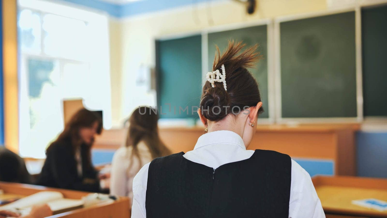 School girl doing homework at home doing homework with back view of a mother cooking in the kitchen