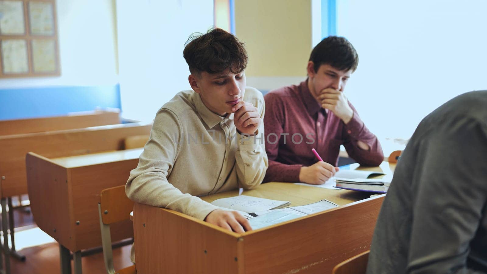 Schoolboys at a desk during class. The boy eats an apple. by DovidPro