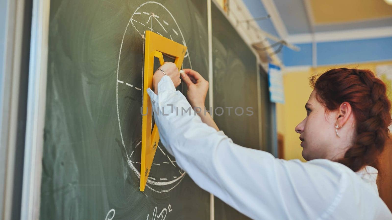 A red-haired schoolgirl draws geometric shapes on the board