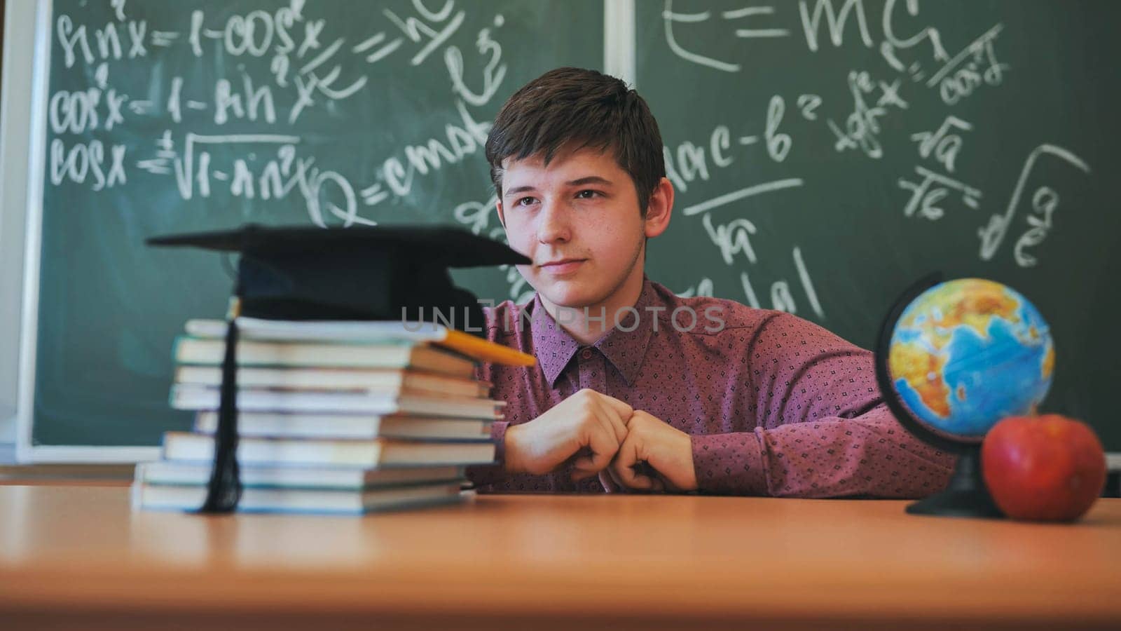 Portrait of a high school student against a background of blackboard, globe and books with cap. by DovidPro