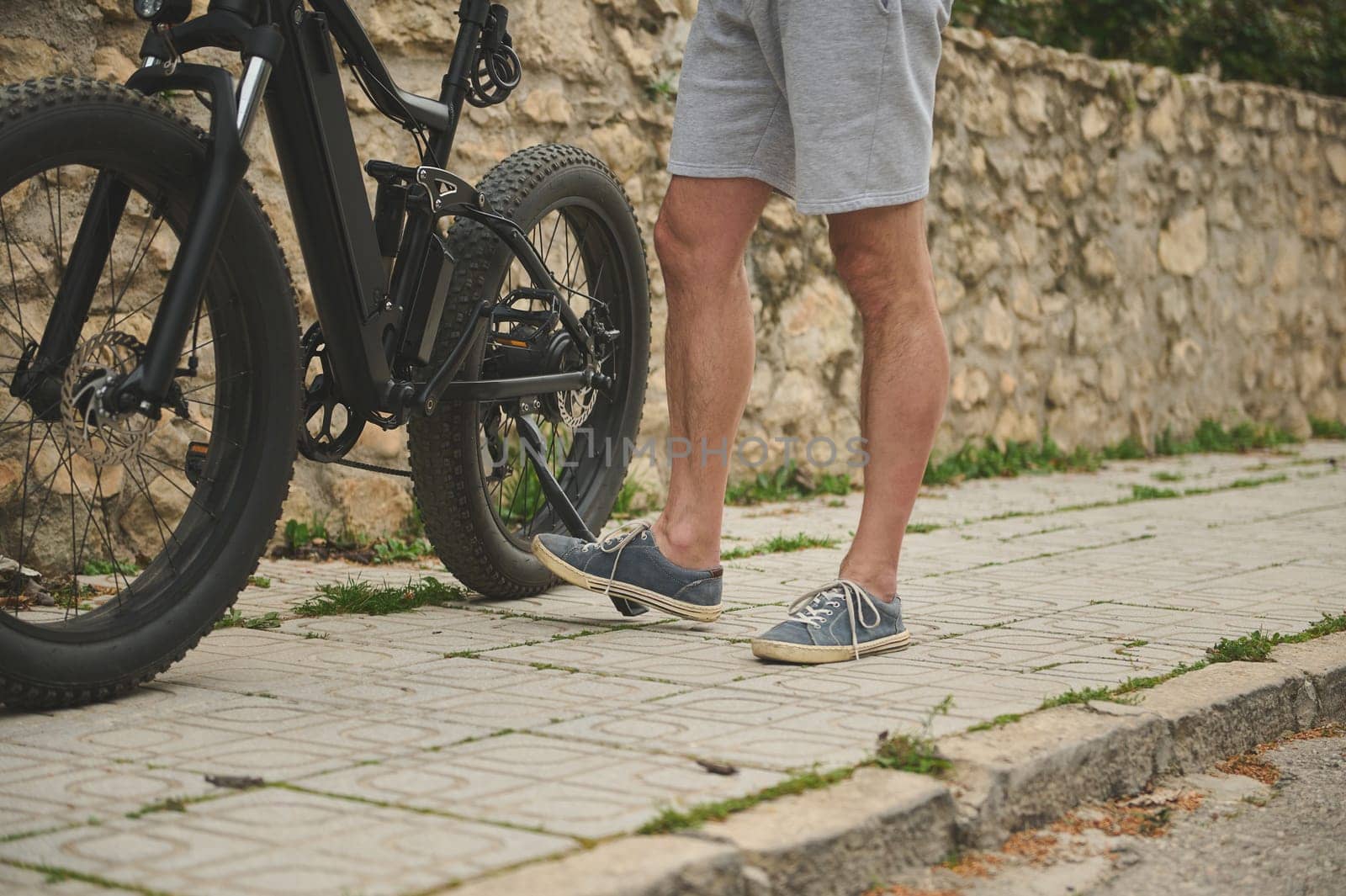 Close-up legs of a cyclist in sports shoes, pushing his bike while walking along the street. Man using e-bike as ecological sustainable mode of urban economic transport. People. Lifestyle. City life