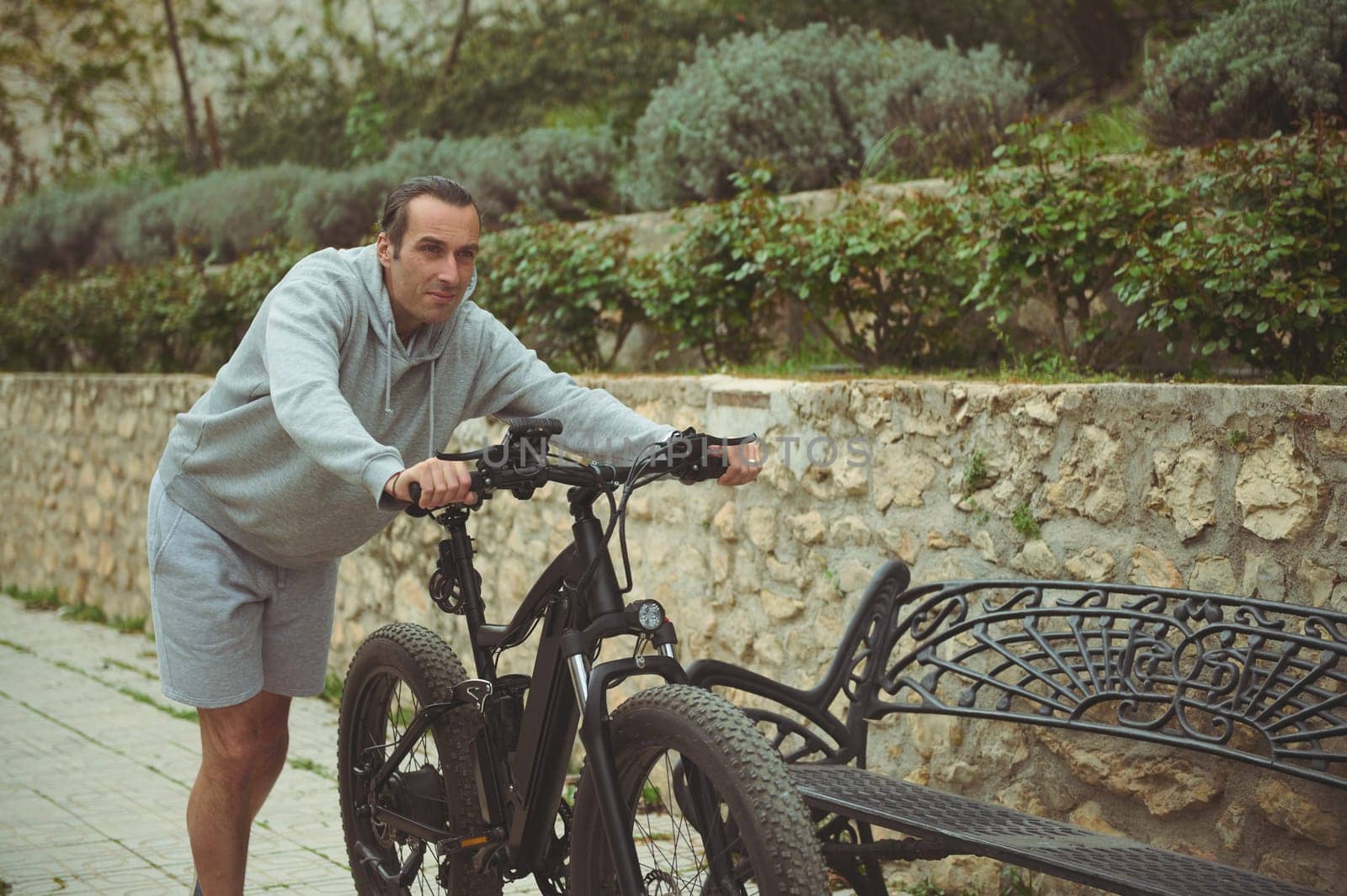 European young man pushing his electric mountain bike up the street. Active lifestyle. Sport. Adventure travel on bicycle. Using el-bicycle ad ecologically friendly mode of urban transport