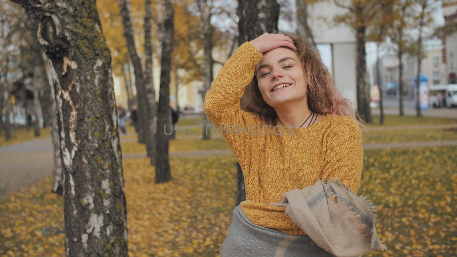 A red-haired, curly-haired girl twirls in the street in the fall