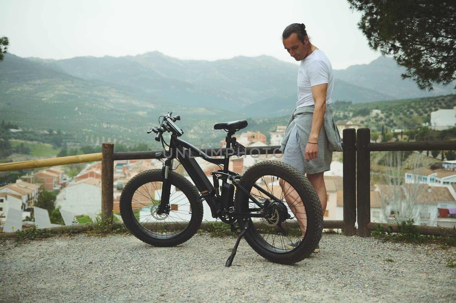 Caucasian man standing with mountain bike on the top of hill, relaxing while cycling in the nature outdoors by artgf