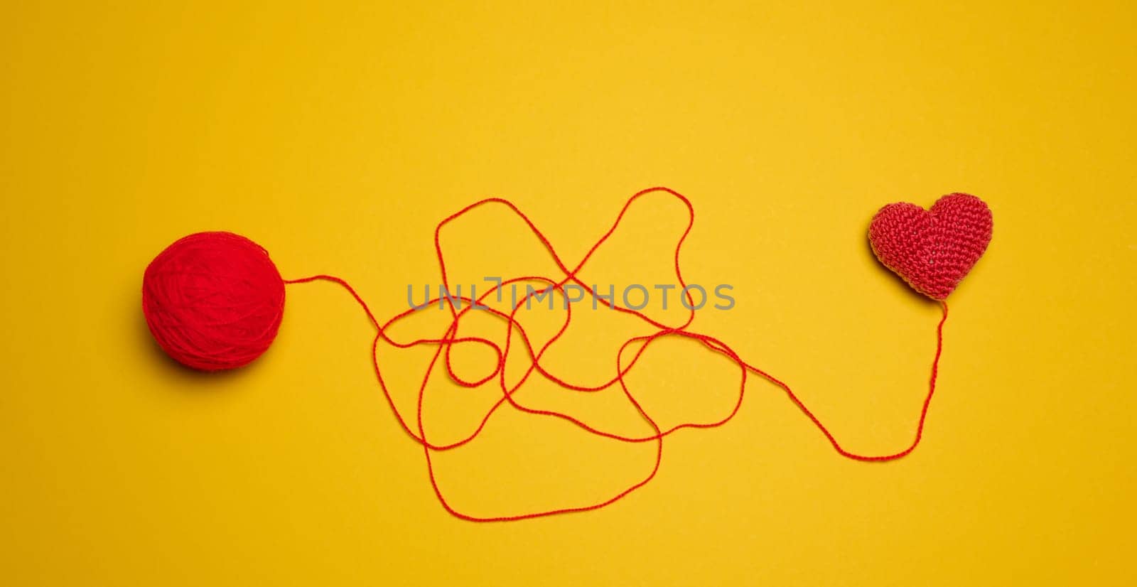 A ball of thread and a knitted red heart on a yellow background, top view by ndanko
