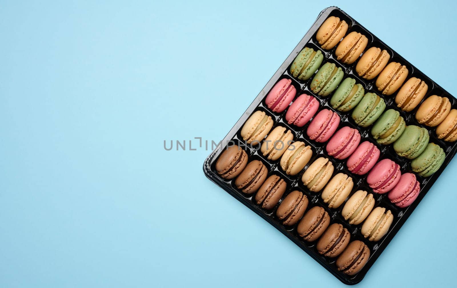 Multi-colored macarons on a blue background in a plastic box, top view. Copy space