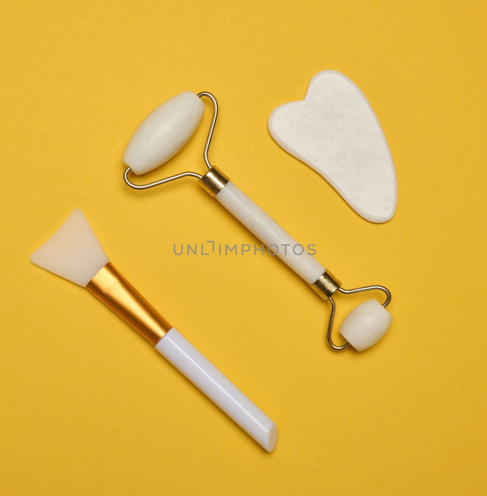 White jade gouache massager and massage jade roller on a yellow background by ndanko