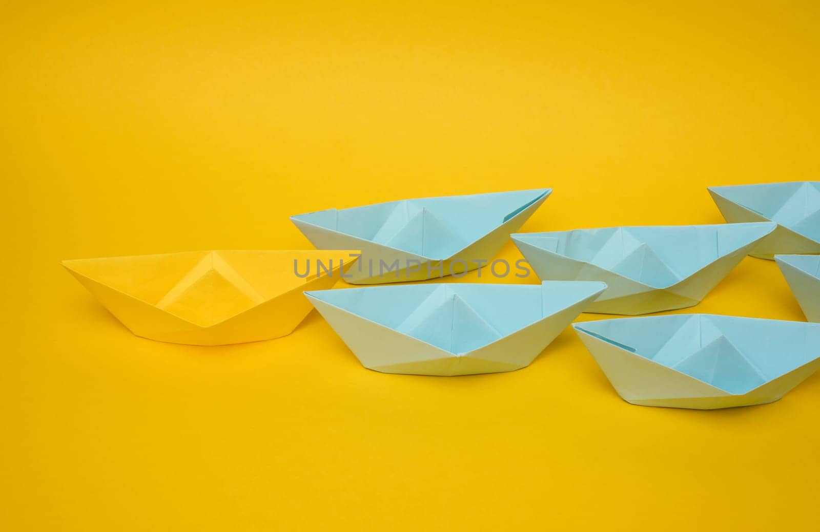 Group of blue paper boats follow yellow against a yellow background. Strong leader concept, mass manipulation. Starting a business with a well-coordinated team by ndanko