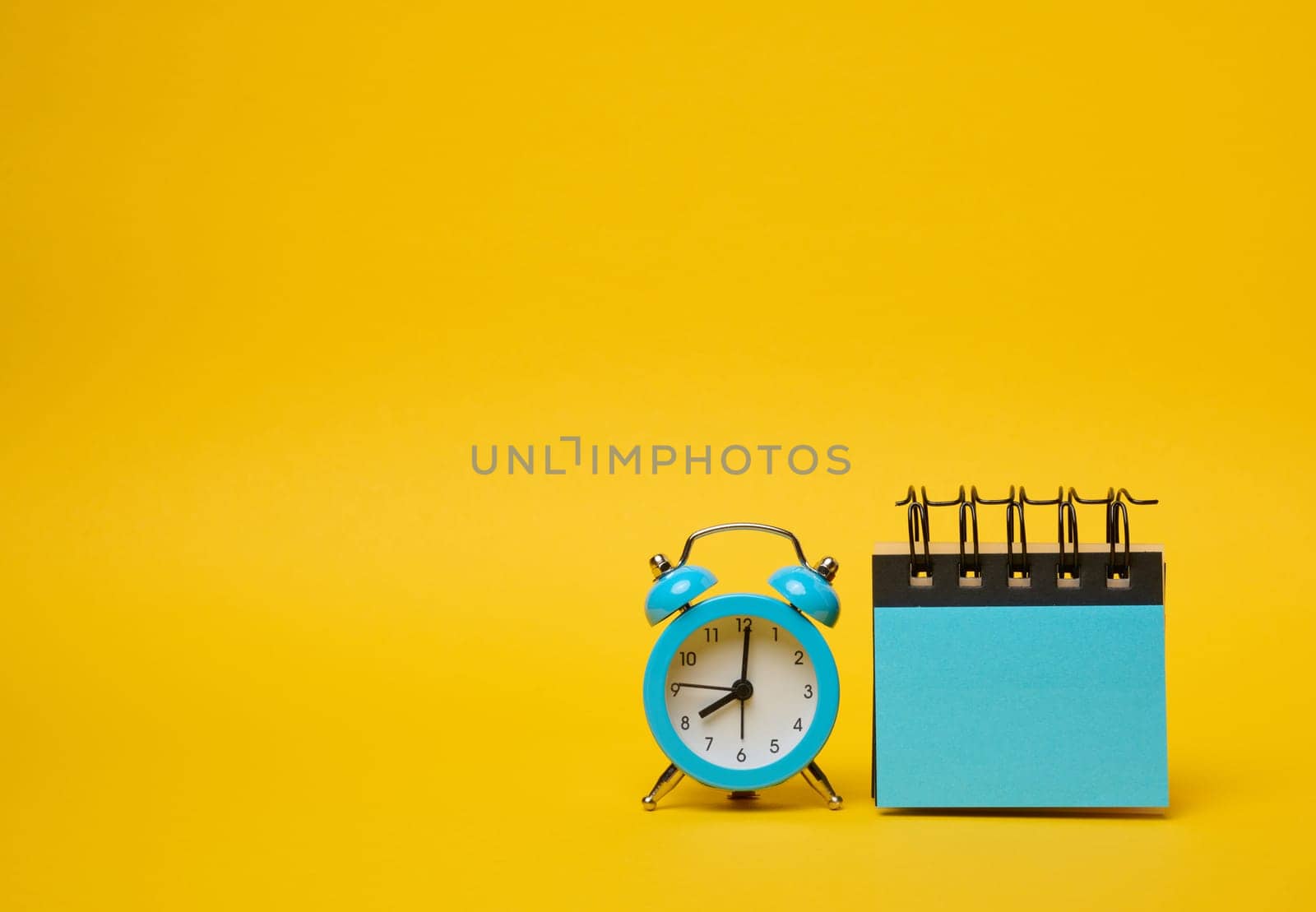 Round alarm clock and blue stickers on a yellow background. Copy space