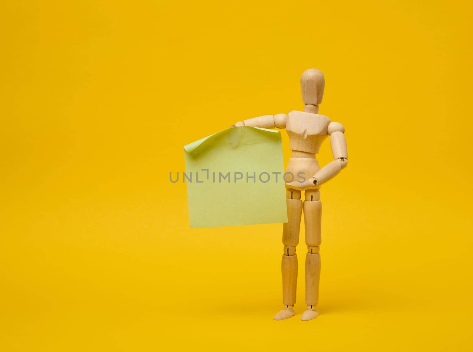 Wooden puppet puppet holding blank sticker sheet on yellow background by ndanko