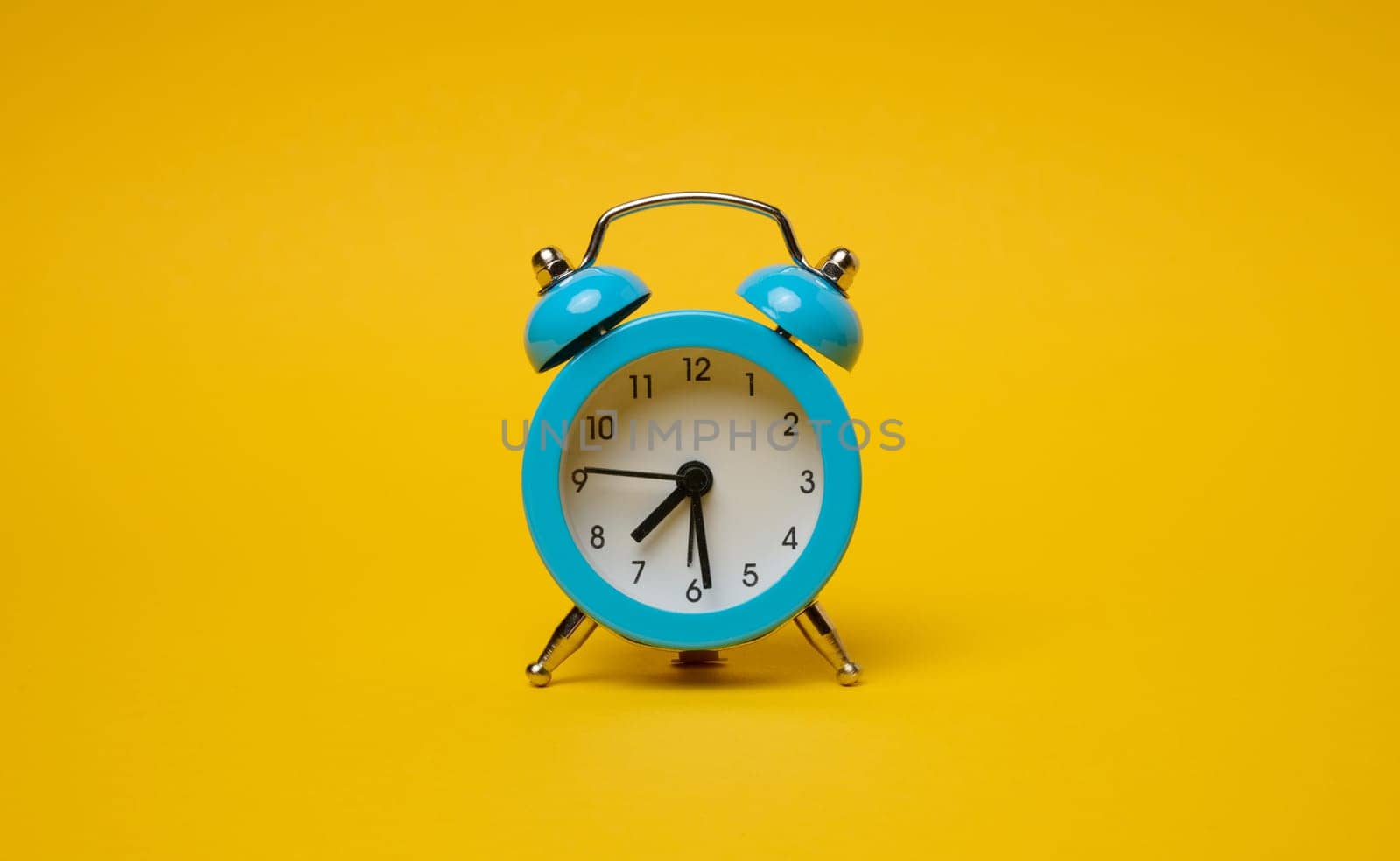 Round alarm clock on a yellow background, half past seven in the morning. 