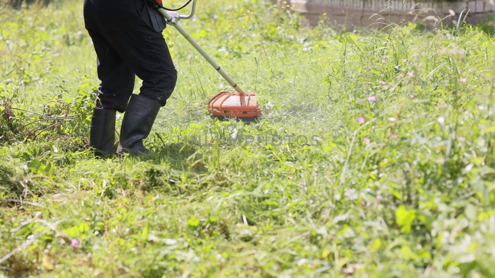 A man mows the grass with a trimmer on a summer day in the countryside. by DovidPro