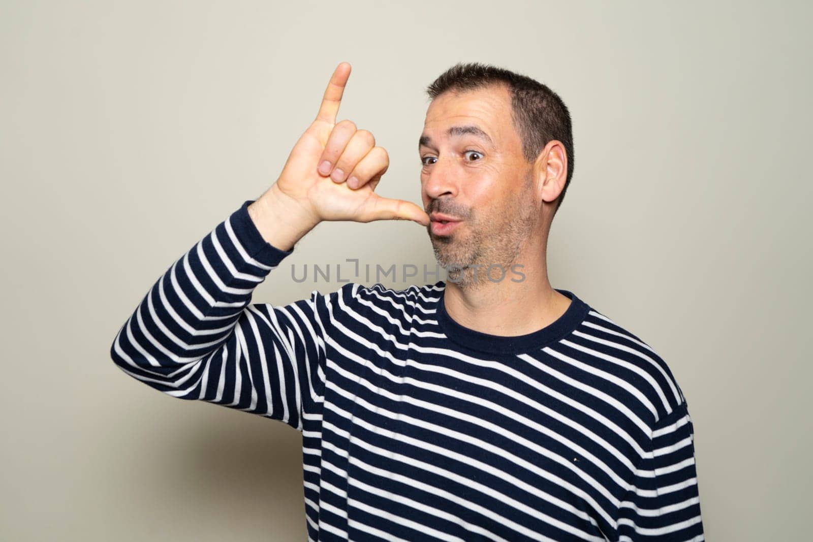 Hispanic man with beard in his 40s wearing a striped sweater making the gesture of being drunk isolated on beige studio background.