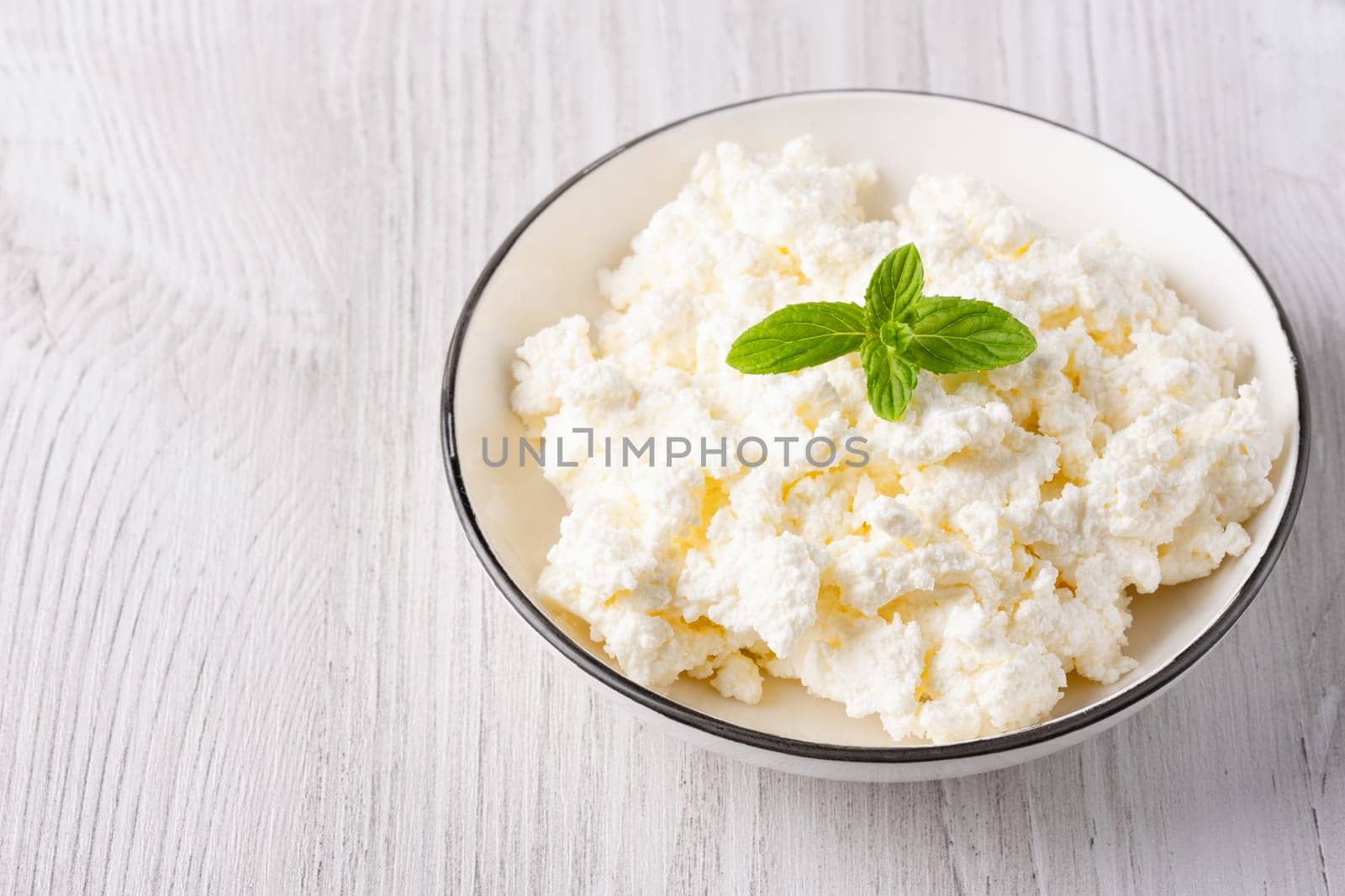 Cottage cheese in a plate on a white table, with copy space for text.