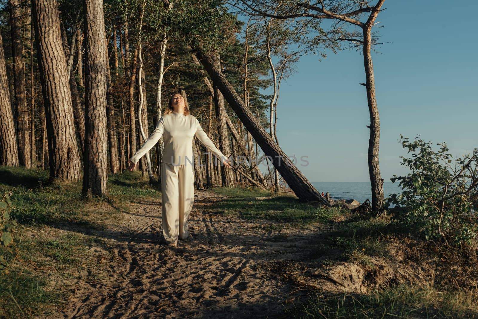 A woman dressed in white clothing is walking down a path, surrounded by nature.