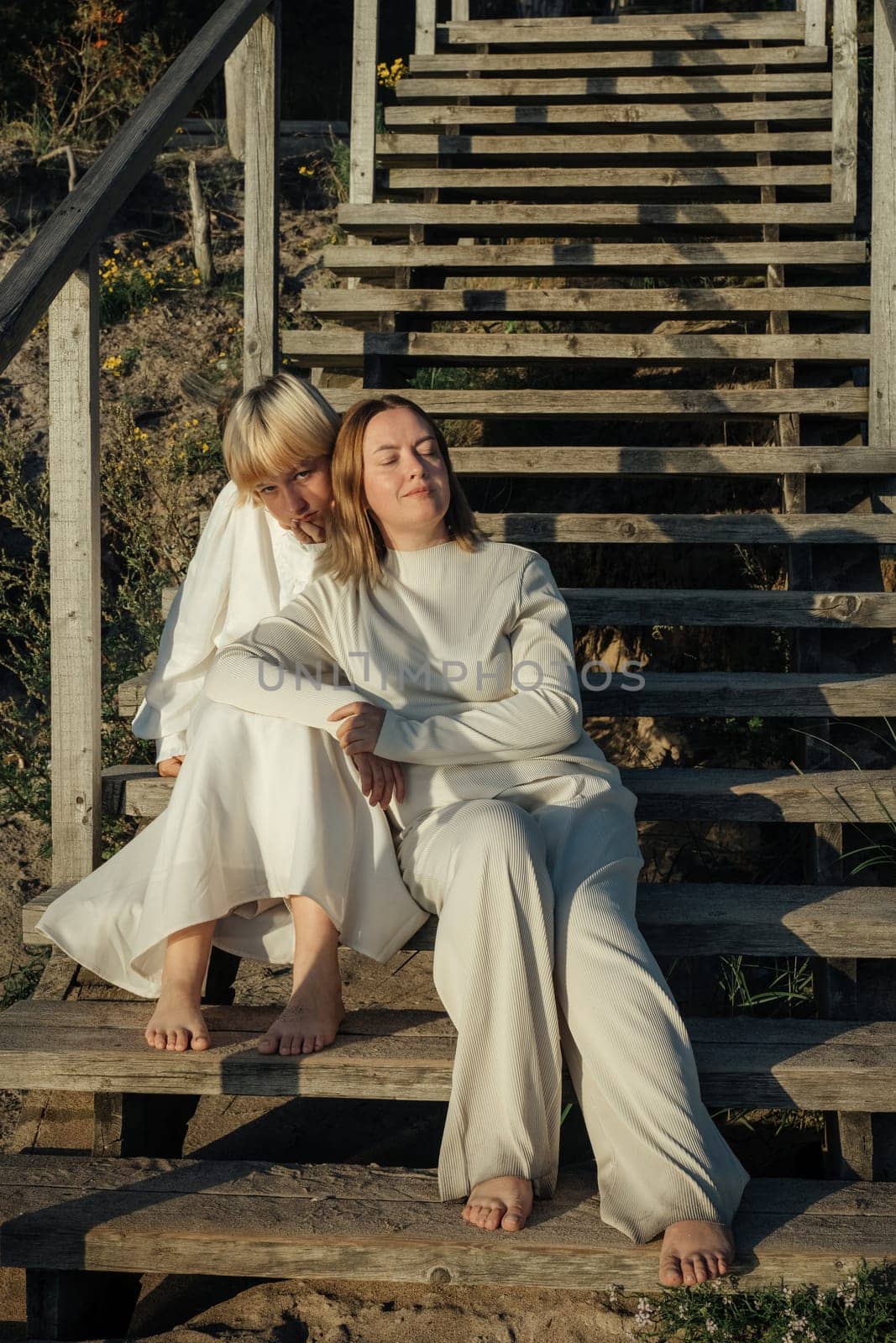 Two sisters sharing a tender moment as they embrace on the steps of a weathered wooden staircase, bathed in the warm glow of the setting sun.