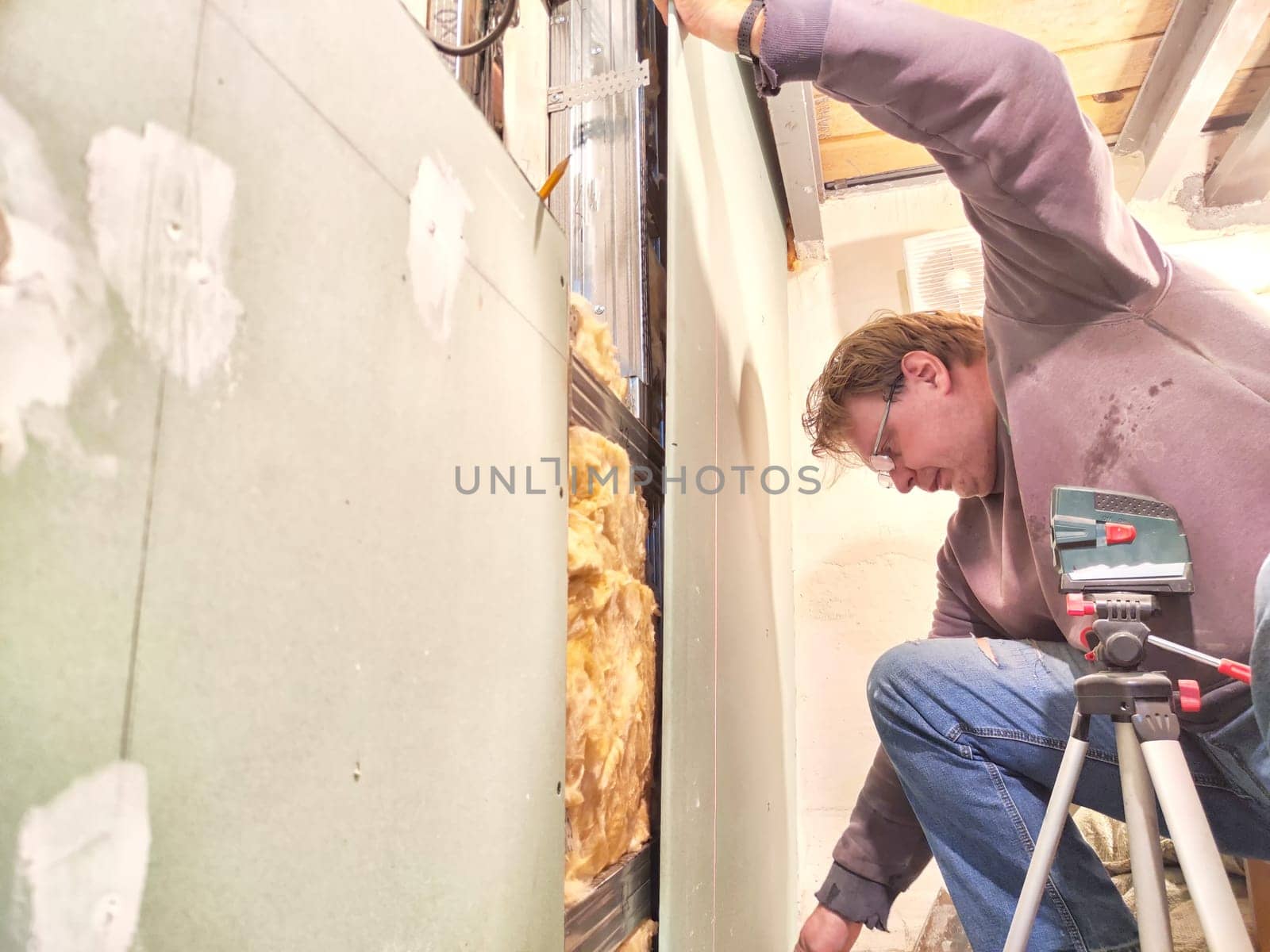 Professional Installs Drywall During Home Renovation. A skilled worker measures and secures drywall in a home under renovation