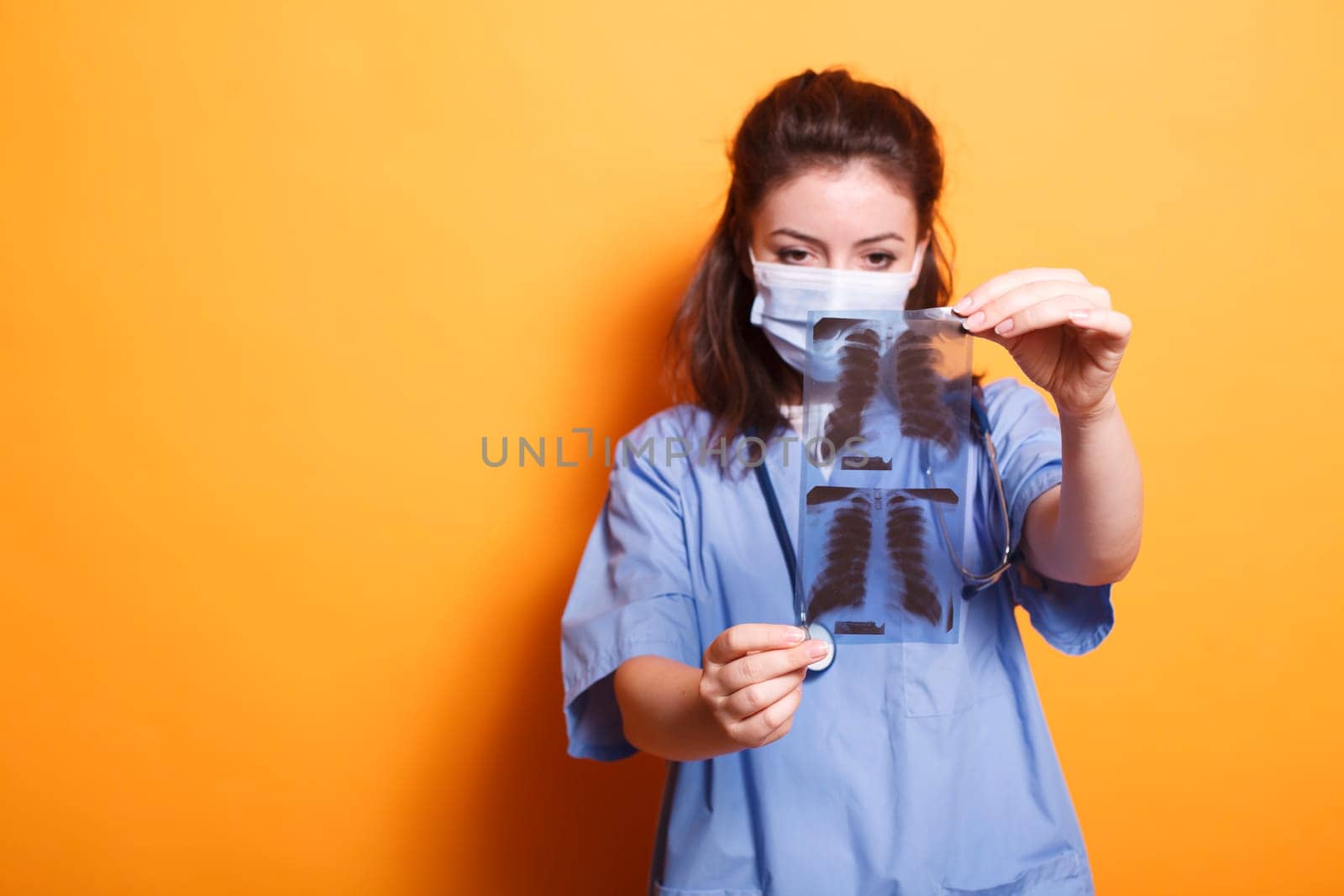 Portrait of doctor holding x-ray scan in front of the camera while wearing coronavirus mask. During covid19 epidemic, nurse practitioner examines the findings of chest radiography.