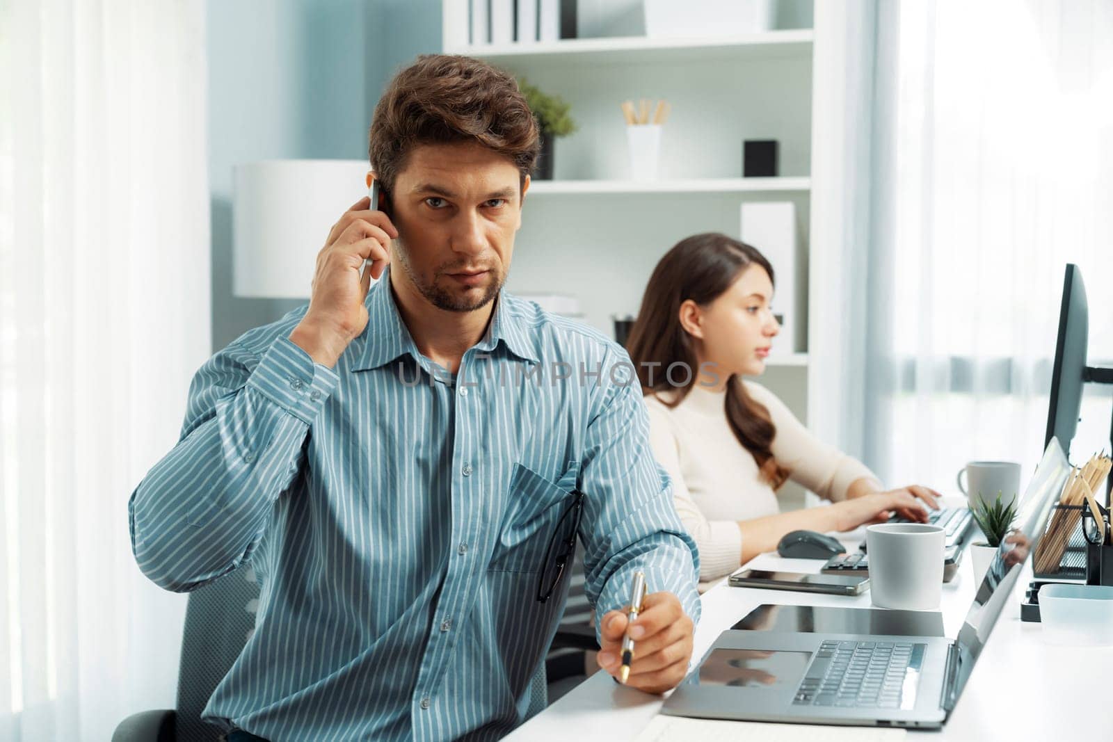 Office worker smart man using phone call to customer or manager, looking at camera photo shooting portrait business pose profile with beautiful coworker at modern office at morning time. Postulate.