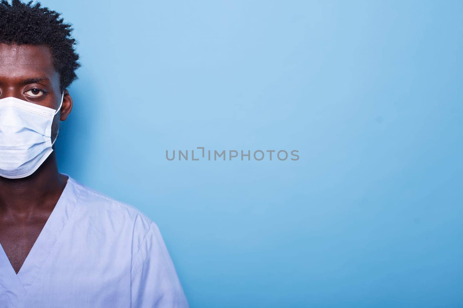 Close up of young man's eye while wearing a face mask for coronavirus protection. Face of black individual in scrubs with a mask for healthcare, standing against an isolated background.