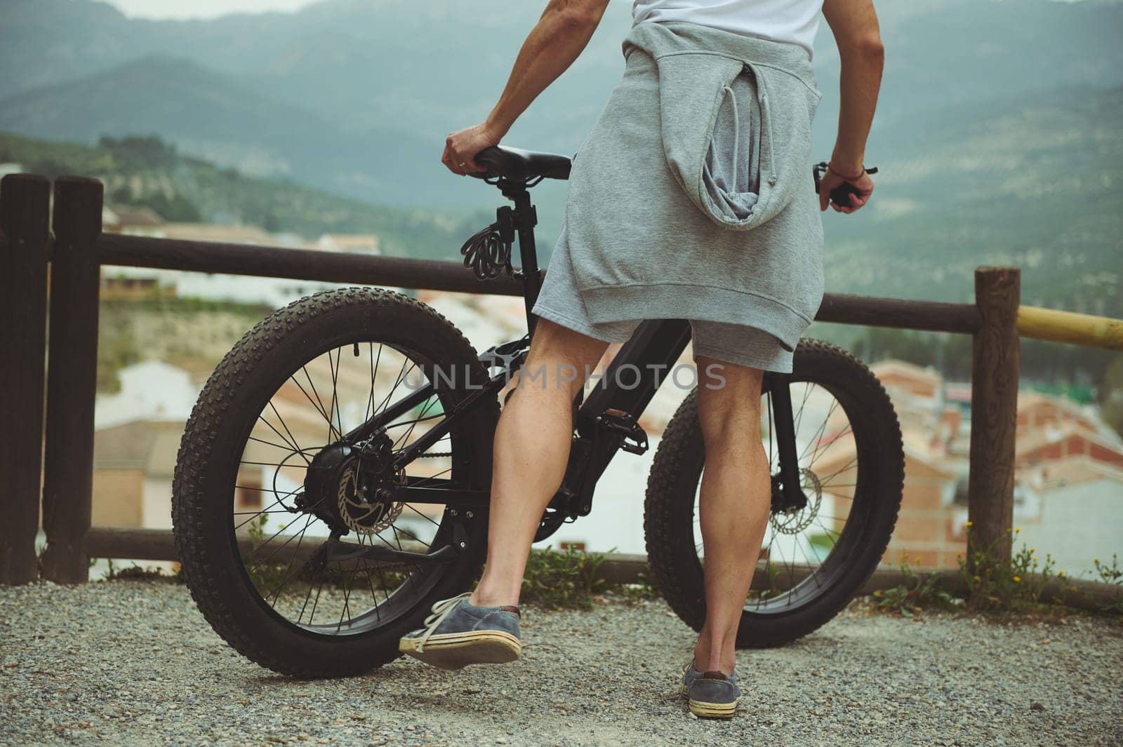 Cropped portrait of a young man cyclist, standing near his electric bike, having a break after biking in mountains. People. Active healthy lifestyle. E-bike as sustainable, eco friendly transportation