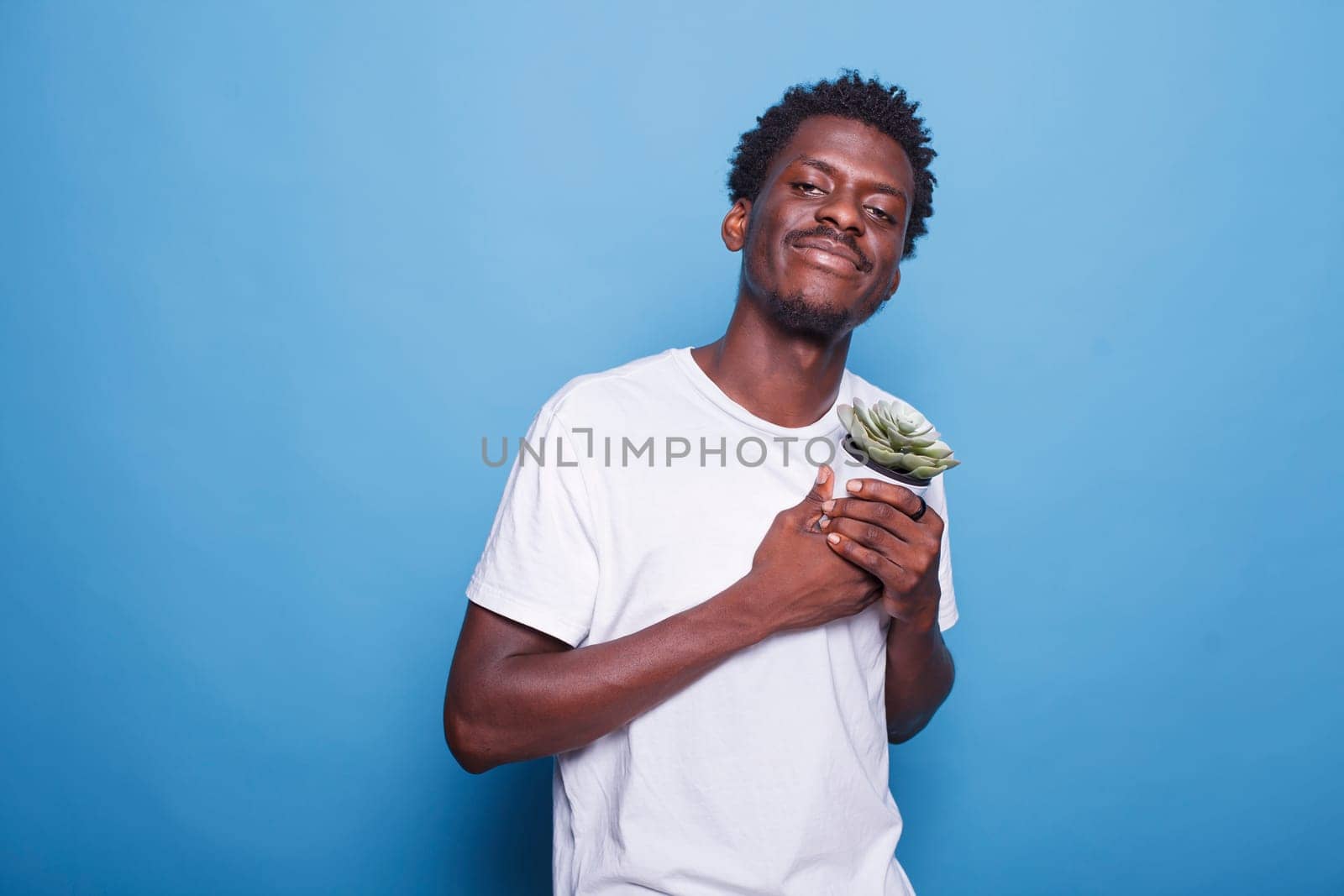 Portrait of black guy carrying container with plants for their botany hobby. Cheerful african american man holding dearly a flowerpot with green leaves for gardening concept and ecology.