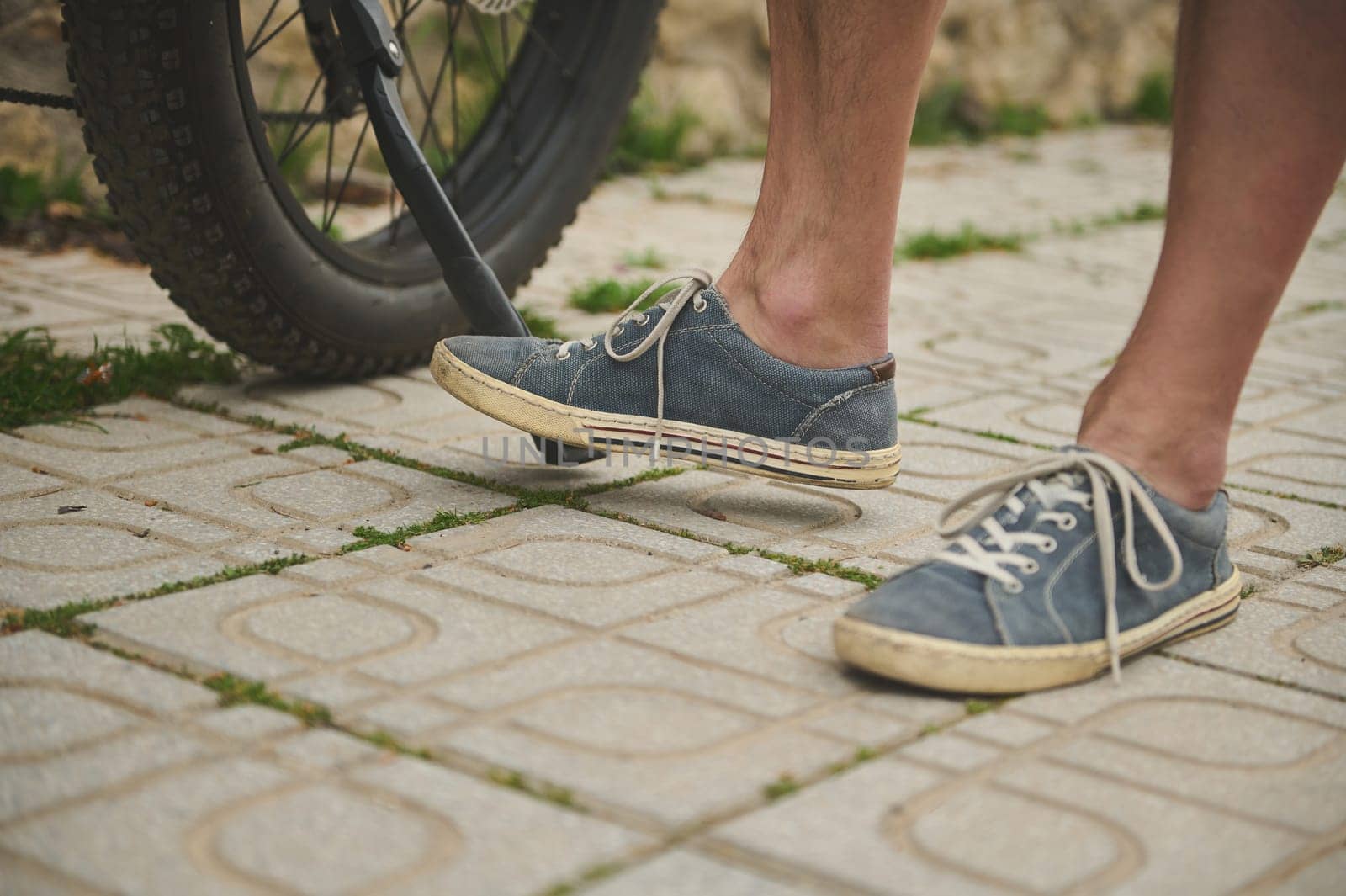 Cropped view male legs in denim sneakers near the electric bicycle wheel. by artgf