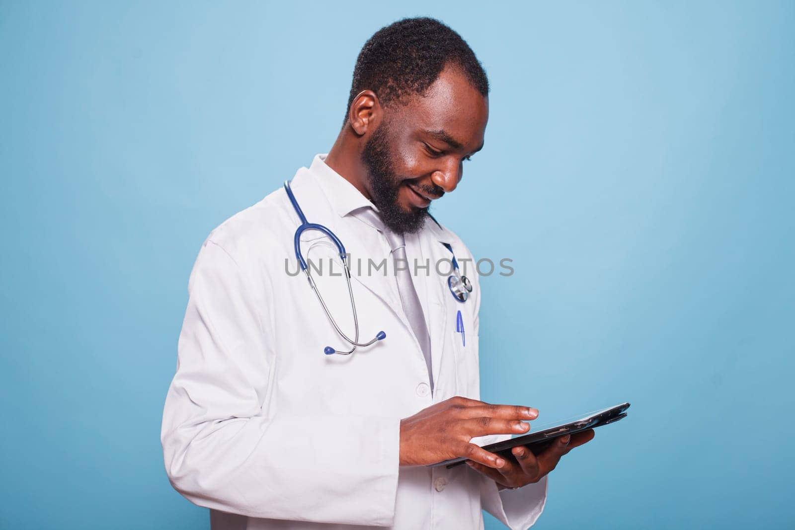 Black man wearing lab coat and stethoscope utilizing modern technology for medical research. African american doctor using digital tablet to review patients healthcare information.