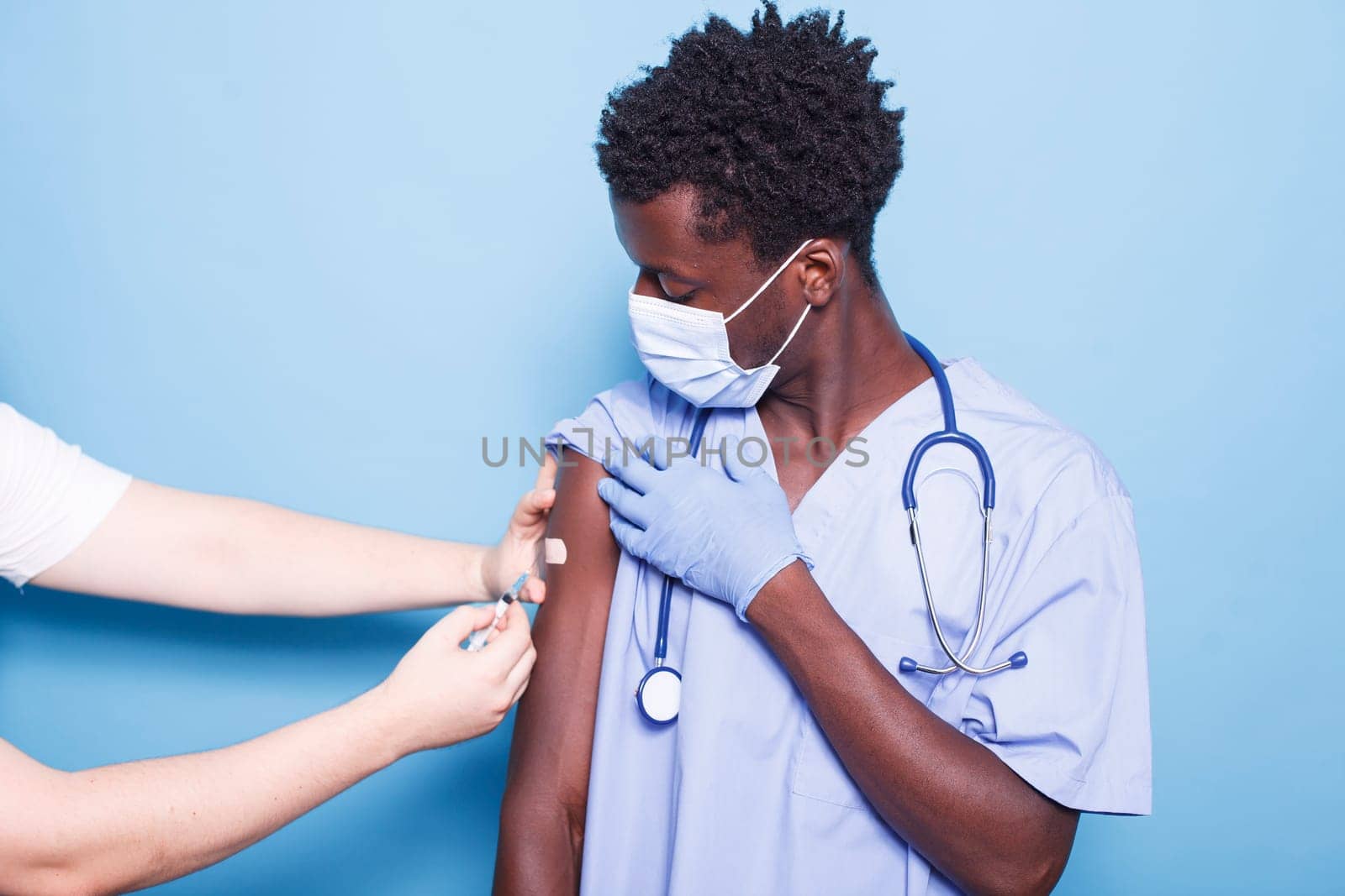 Caucasian person administering vaccine injection to African American nurse against blue background. Close-up of a doctor giving vaccination to black man, ensuring healthcare and covid 19 prevention.