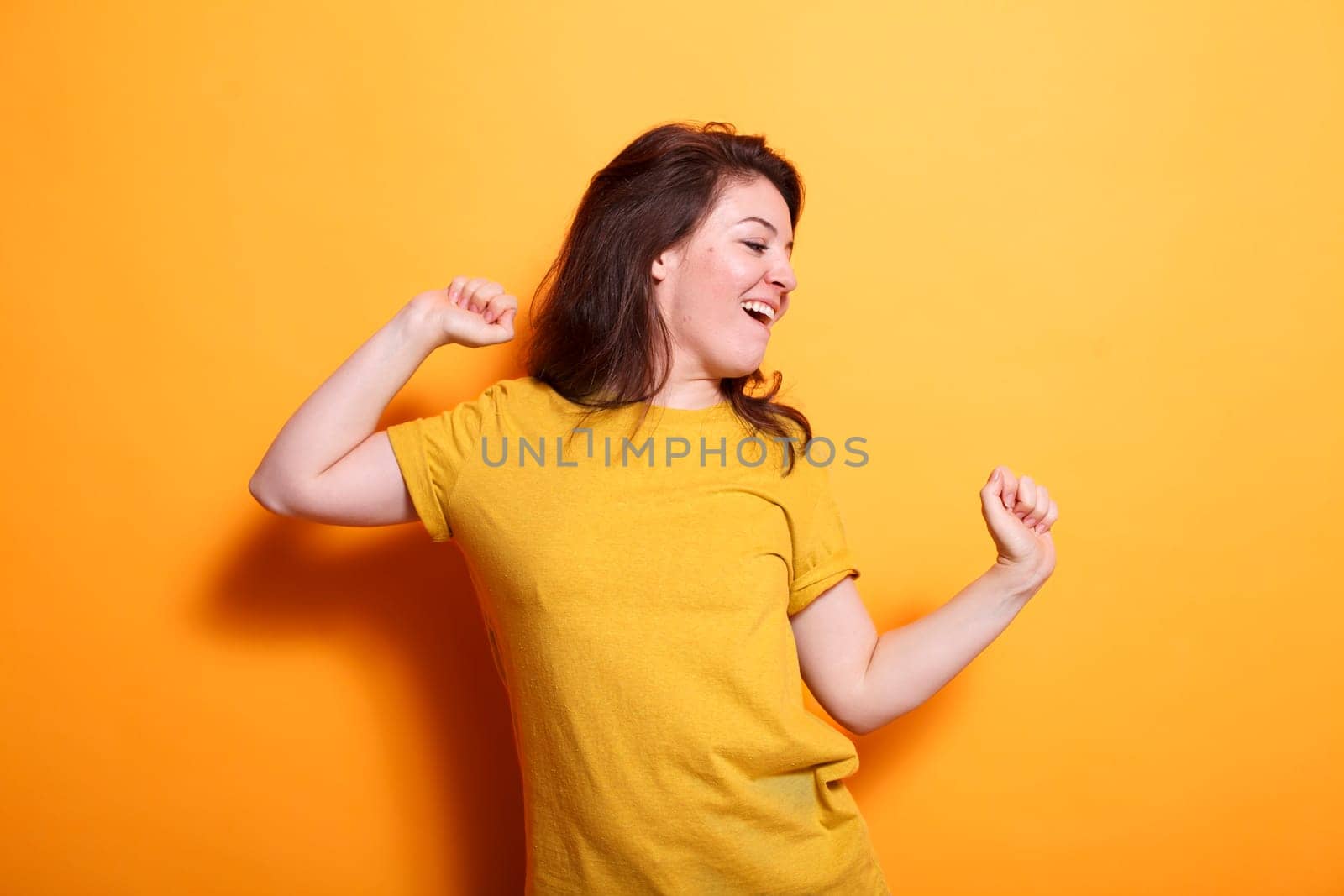 Cheerful woman happily dancing with hands in the air in front of isolated background. Caucasian lady radiating positivity, showcasing dance skills, and enjoying herself during casual photo shoot.