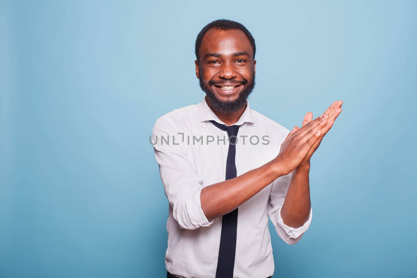 Smiling male adult clapping hands and cheering on job well done, enjoying a significant win. Excited black man expressing his congratulations with an applause gesture and positive response.