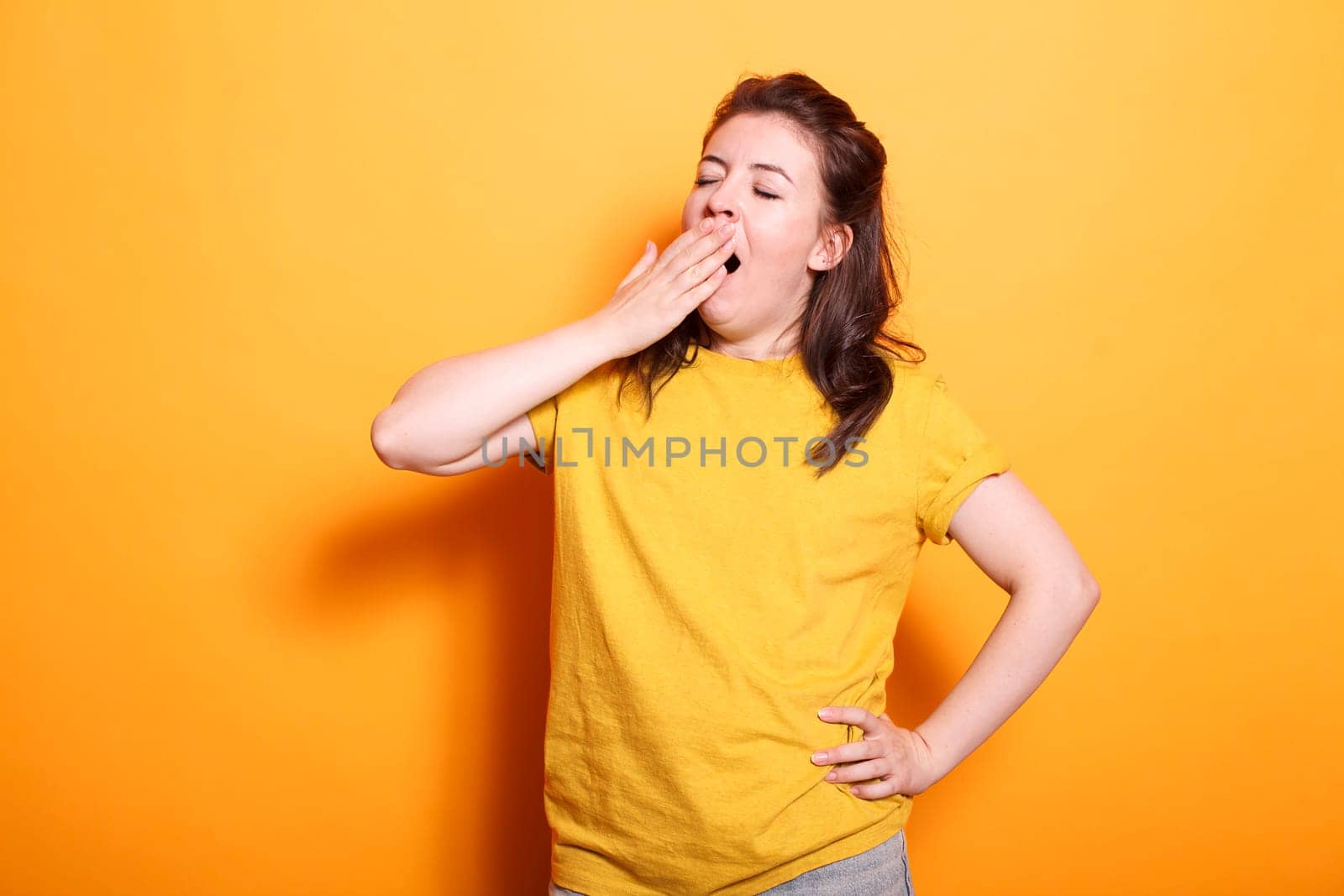 Portrait of caucasian woman yawning and covering her mouth, feeling sleepy in studio. Tired female person falling asleep while posing and standing over isolated background.