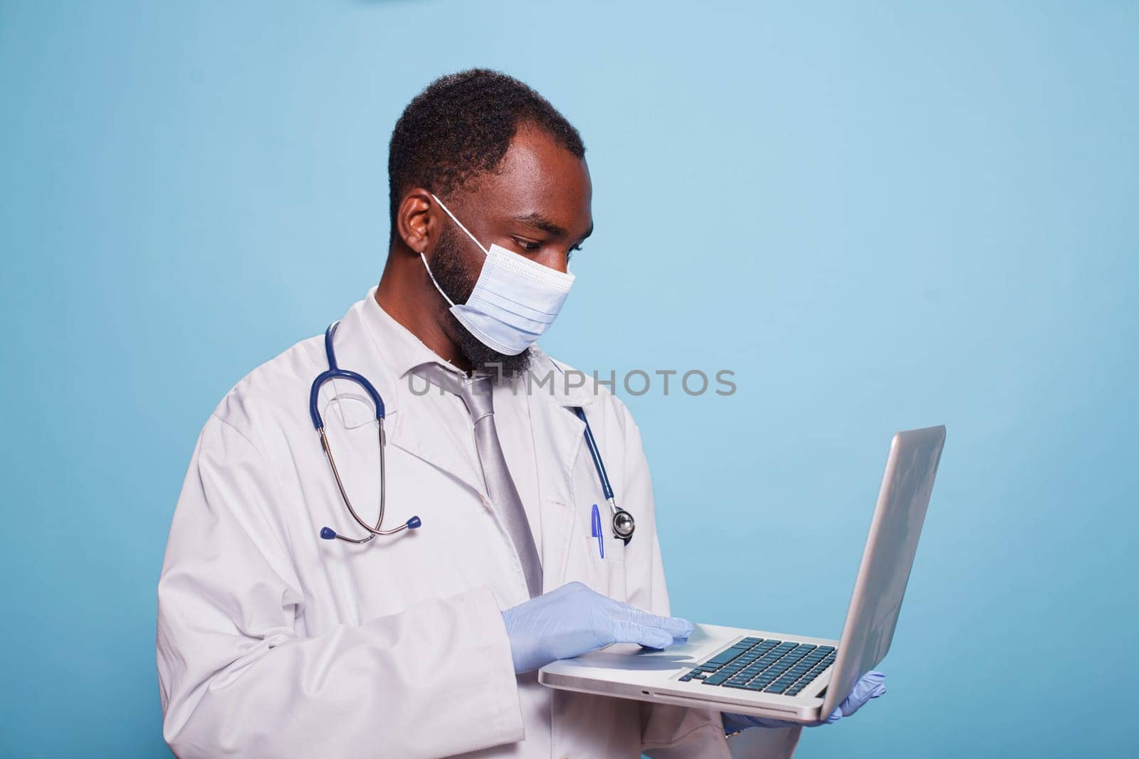 Physician wearing face mask uses laptop by DCStudio