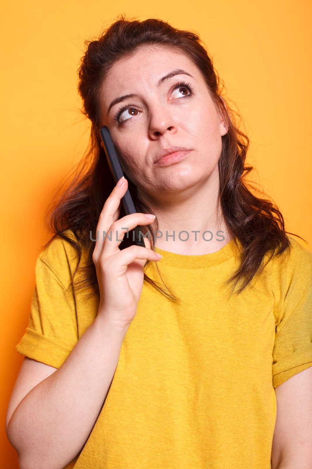 Portrait of female individual having important phone call conversation in front of isolated background. Close-up of woman in thoughts while talking on her mobile device with friends and family.