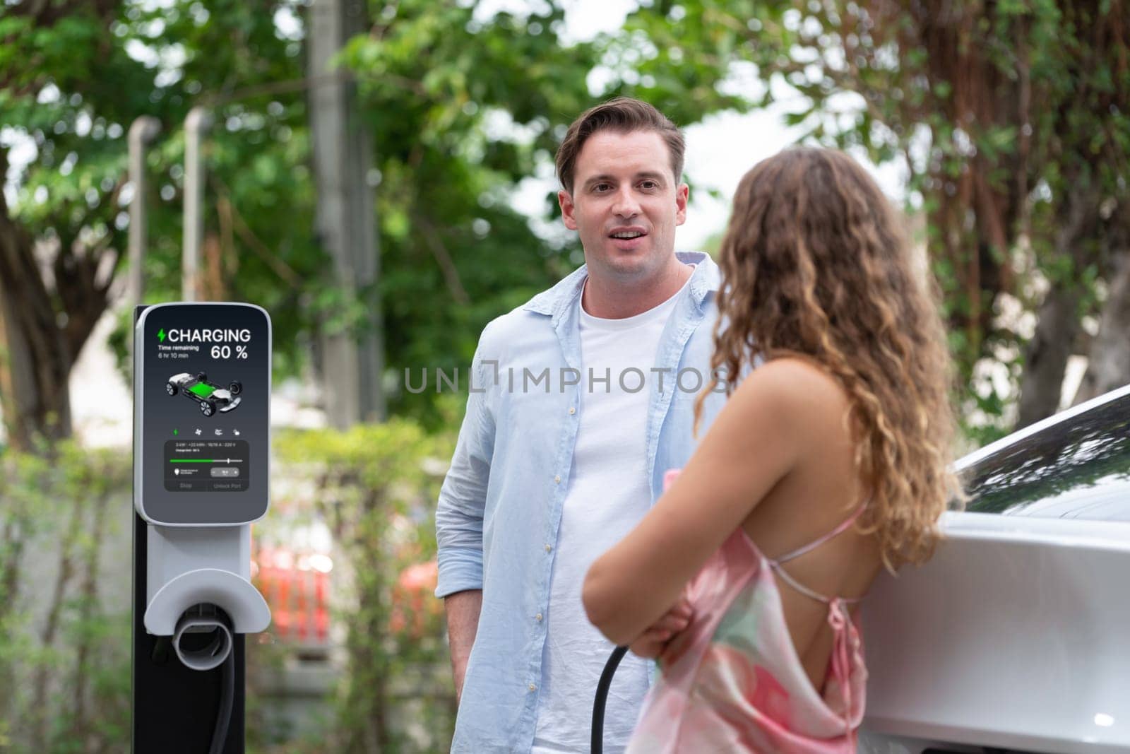 happy couple recharge electric vehicle from EV charging station. Synchronos by biancoblue