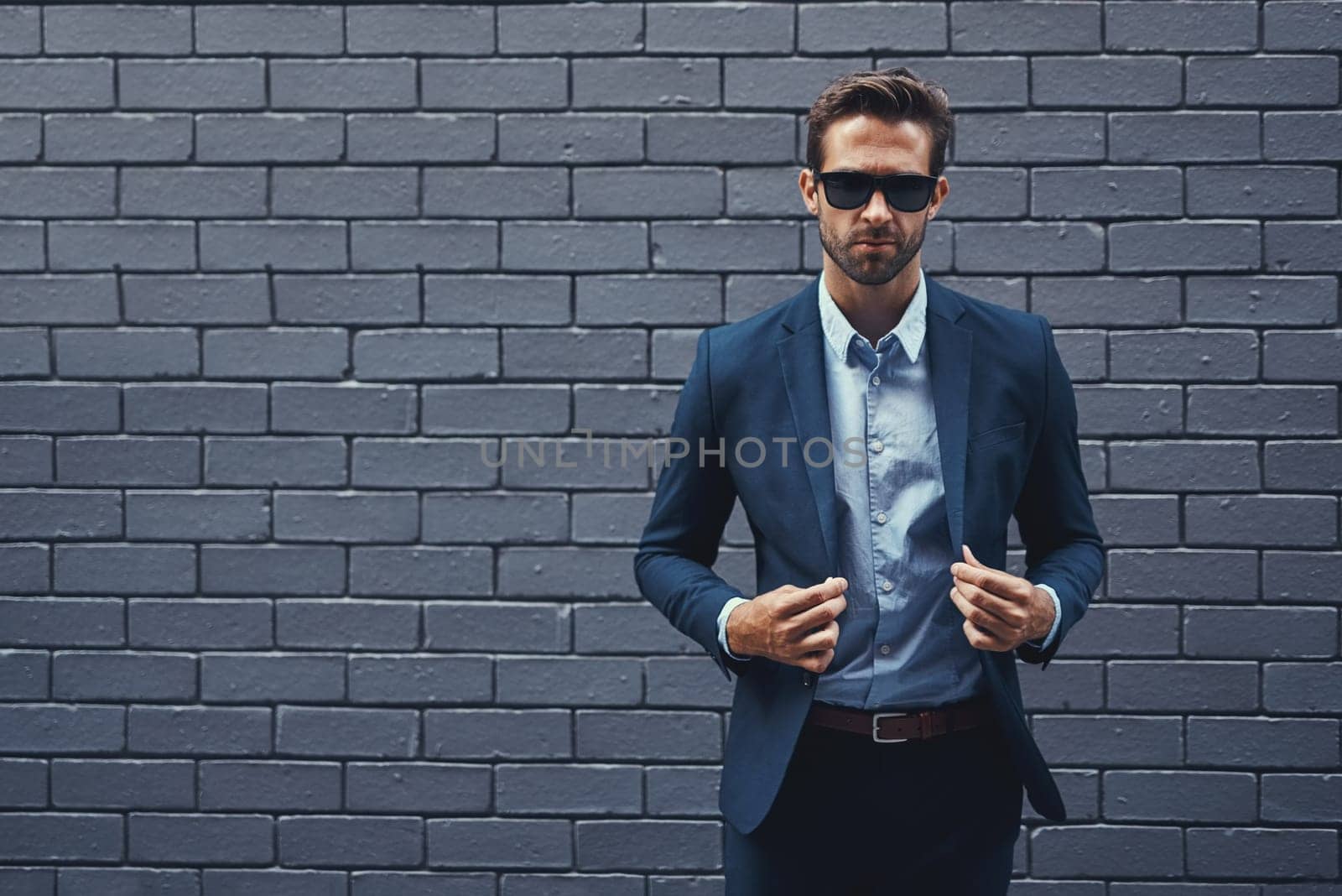 Confident, man and wall in suit with sunglasses for fashion, style and trendy in outdoor. Male person, pride and project manager for work, corporate and career on grey background in New York City by YuriArcurs