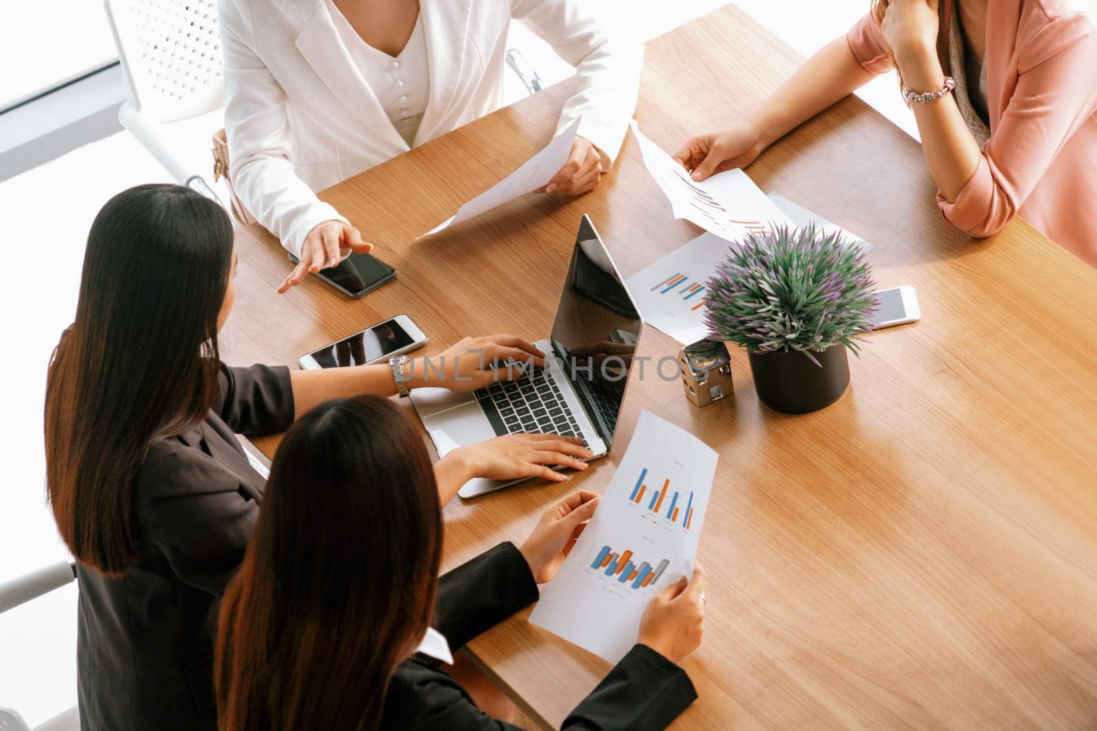 Businesswoman in group meeting discussion with other businesswomen colleagues in modern workplace office with laptop computer and documents on table. People corporate business work team concept. uds