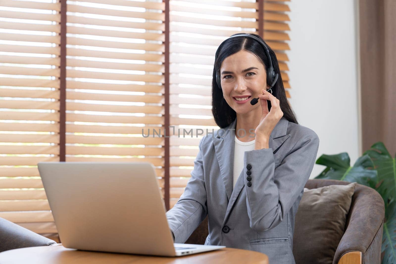 Female call center operator or customer service helpdesk staff working on workspace while talking on the headset to provide assistance for customer. Professional modern business service. Blithe