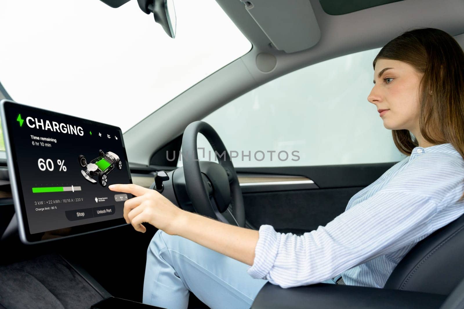Young woman inside the vehicle, checking EV vehicle's application on battery recharging electricity status display on smart monitor screen in modern EV car on her road trip journey. Exalt
