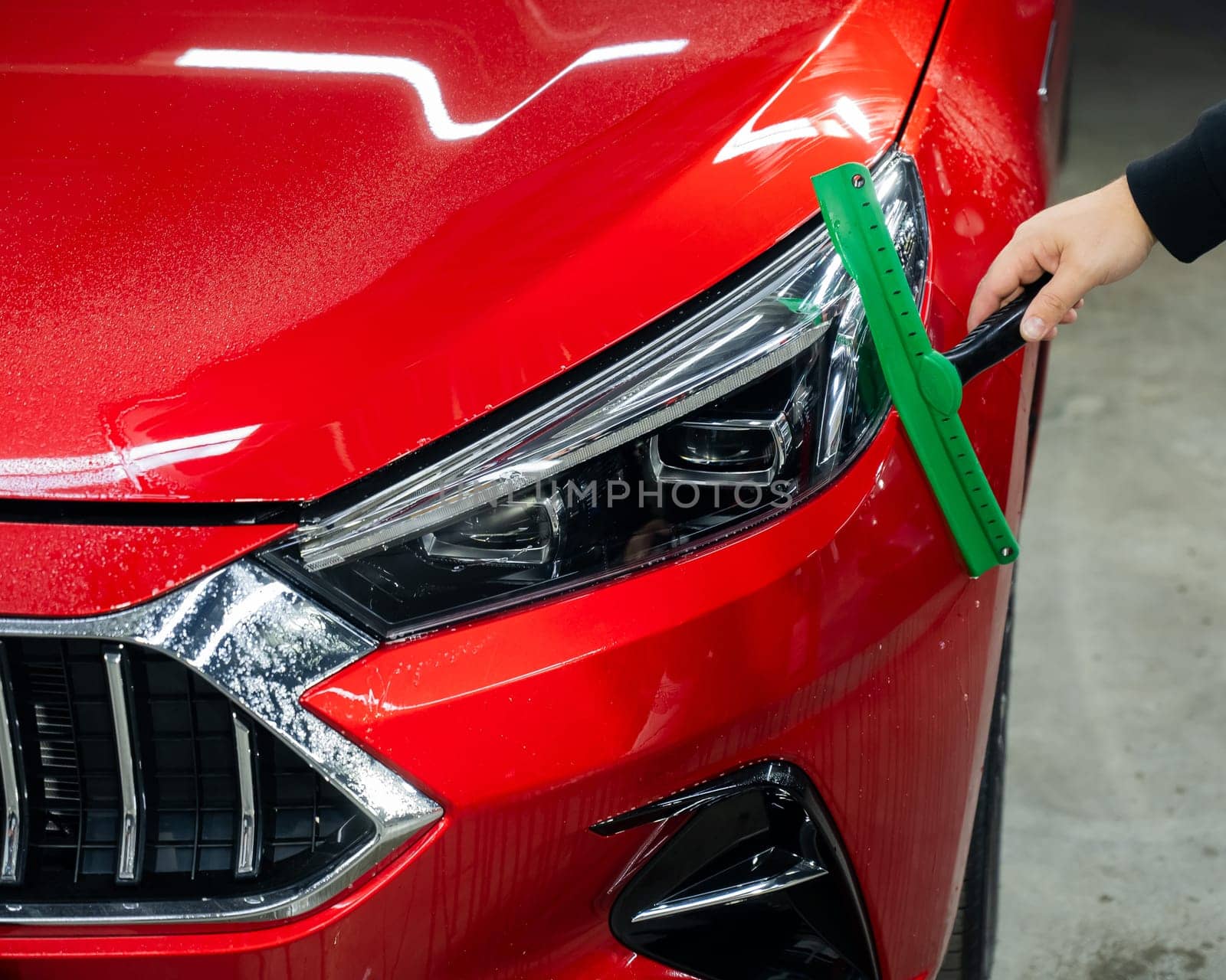 A man washes the headlights of a red car with a scraper